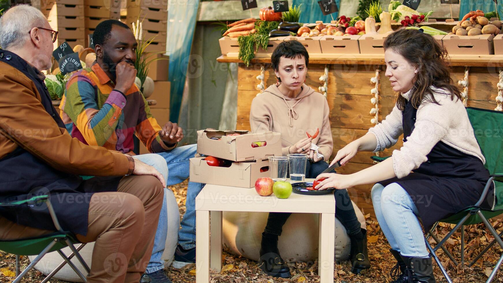 groupe de de bonne humeur gens séance à table et dégustation biologique des produits, en riant à rue nourriture équitable. les clients et local vendeurs en mangeant des fruits et légumes à en plein air rester, produire échantillonnage. photo