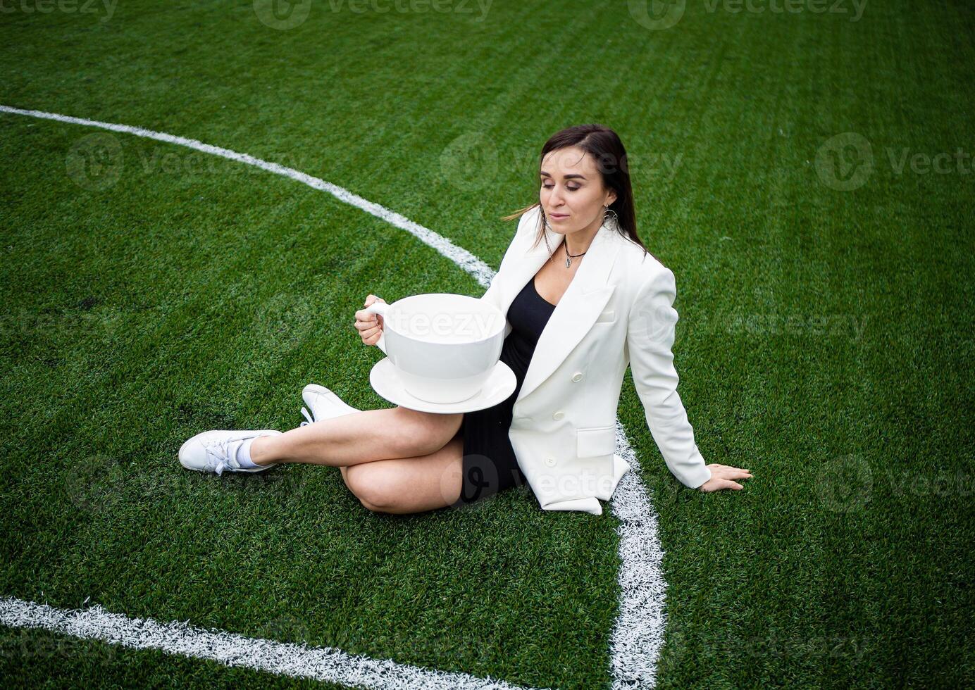 une affaires femme avec une grand tasse, séance sur une vert pelouse dans le parc. photo