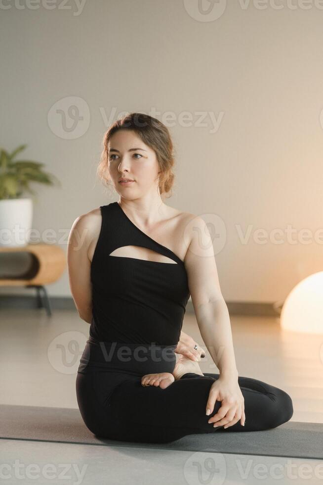 une fille dans noir tenue de sport Est-ce que yoga sur une tapis dans le aptitude pièce photo