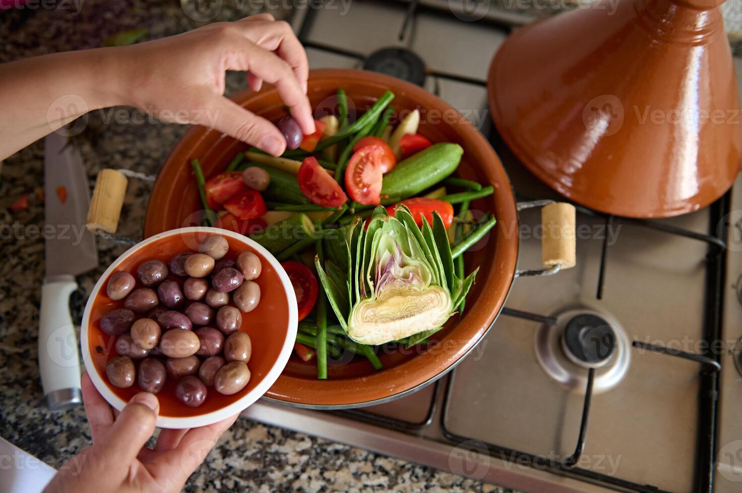 vue de au dessus de femme au foyer ajouter Olives dans une repas tandis que cuisine en bonne santé végétarien repas dans tajine photo