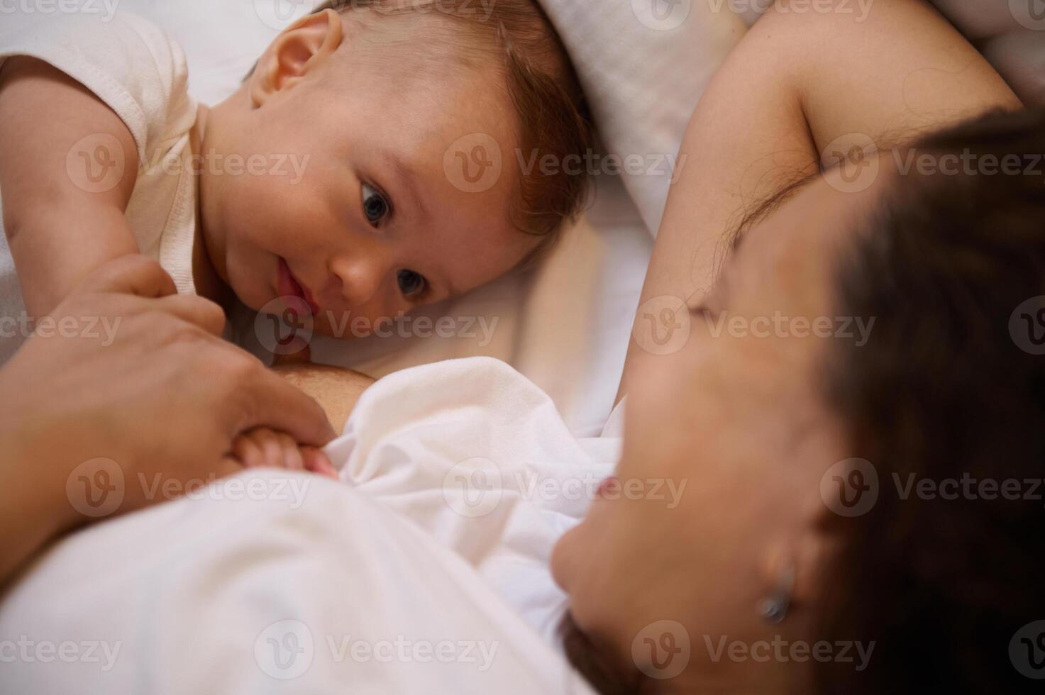 fermer de une mignonne bébé mensonge suivant à le sien mère tandis que elle allaitement maternel lui. photo