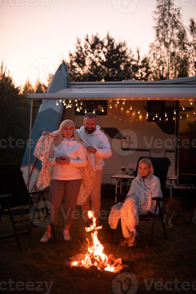 le famille est relaxant ensemble par le feu de camp près leur mobile maison. soir famille vacances photo