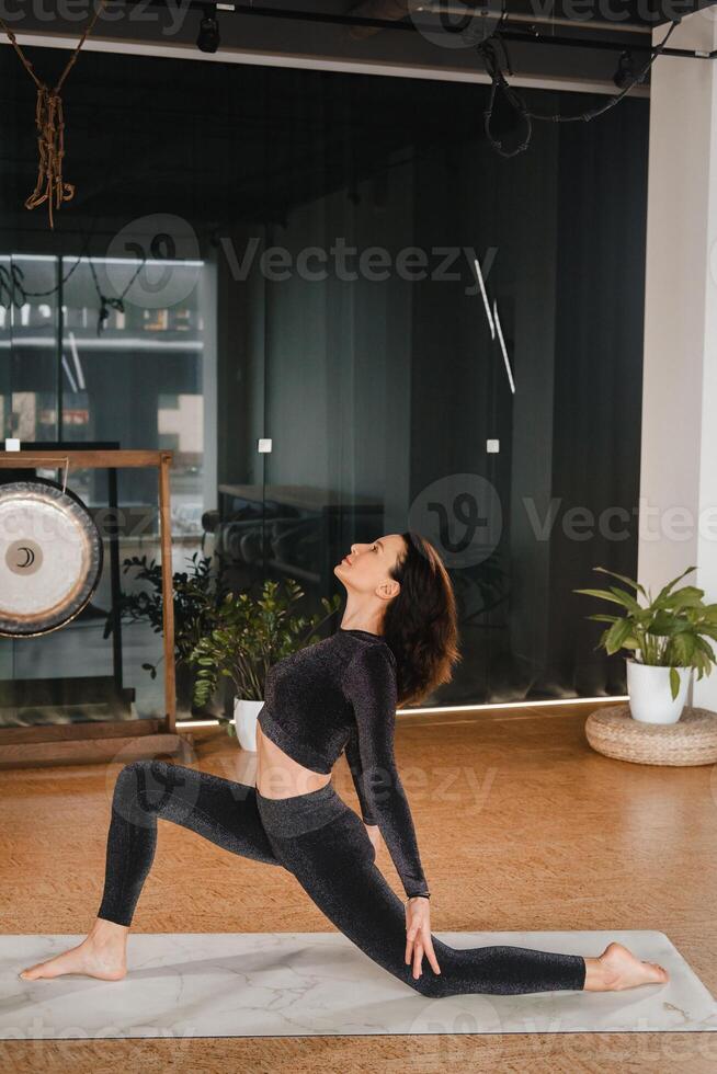 une fille dans une noir des sports uniforme Est-ce que yoga permanent sur une tapis dans le Gym photo