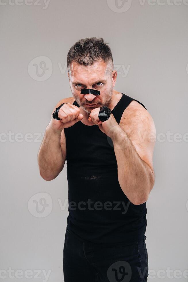 sur une gris Contexte des stands une battu homme dans une noir t chemise à la recherche comme une combattant et en train de préparer pour une bats toi photo