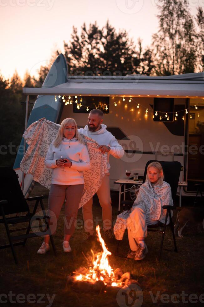 le famille est relaxant ensemble par le feu de camp près leur mobile maison. soir famille vacances photo