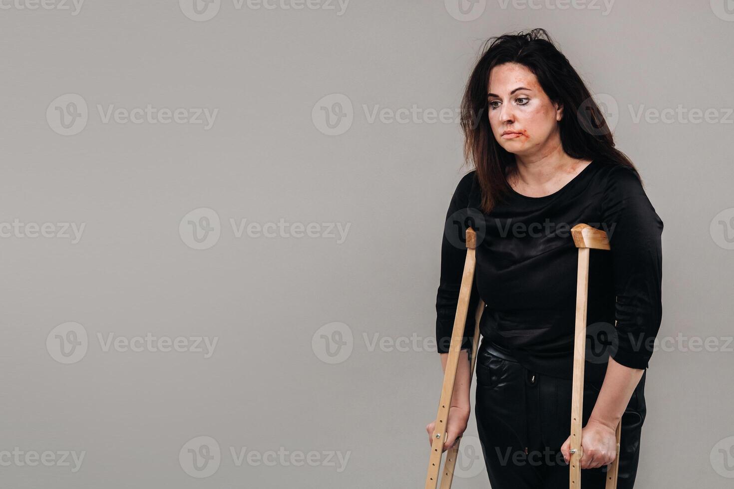 une femme battu dans noir vêtements avec béquilles dans sa mains sur une gris Contexte photo