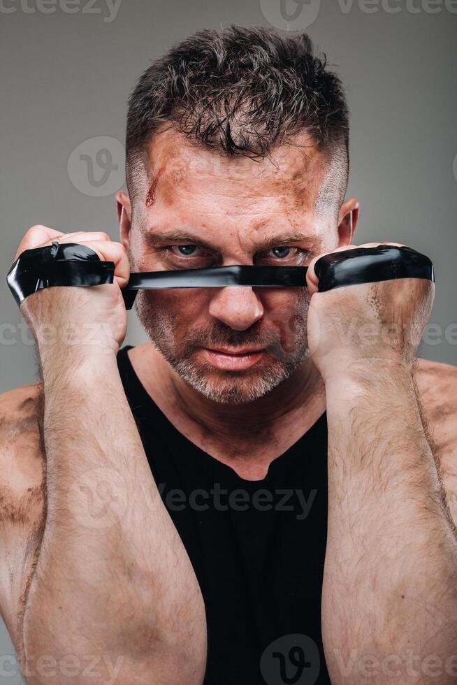 sur une gris Contexte des stands une battu homme dans une noir t chemise à la recherche comme une combattant et en train de préparer pour une bats toi photo