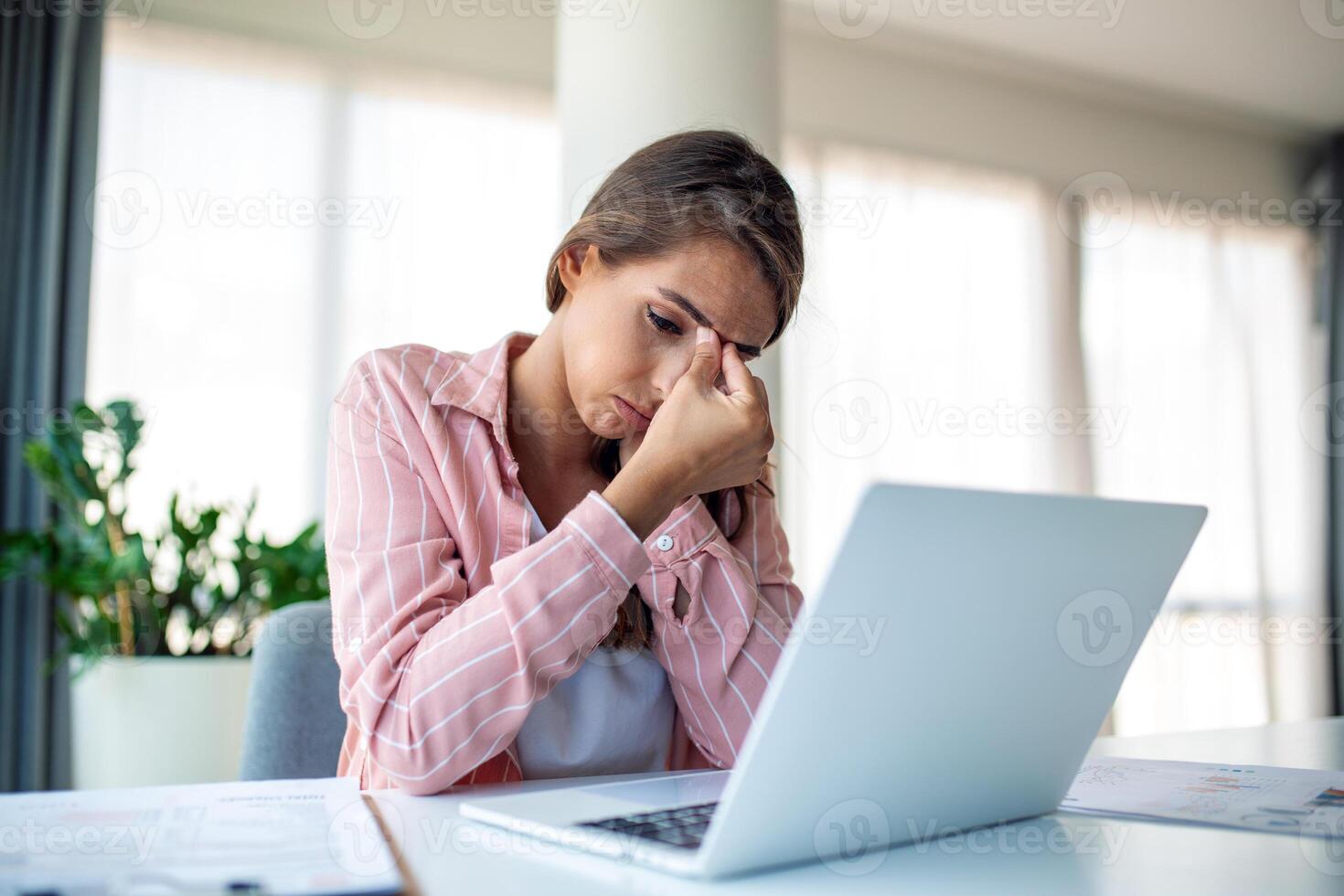 épuisé femme d'affaires ayant une mal de crâne dans sa bureau. surmené femme d'affaires expérience travail fatigue tandis que implantation dans de face de une portable. photo