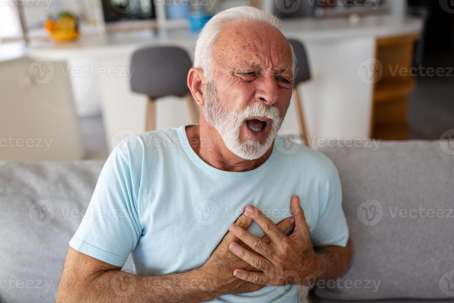 Sénior homme presses main à poitrine a cœur attaque souffre de insupportable douleur, mature homme avec douleur sur cœur dans vivant chambre. Sénior homme Souffrance de mal douleur dans le sien poitrine cœur attaque à Accueil photo