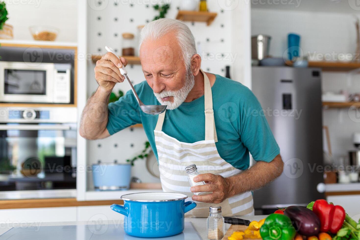 content retraité Sénior homme cuisine dans cuisine. retraite, loisir gens concept. portrait de souriant Sénior homme en portant cuillère à goût nourriture photo