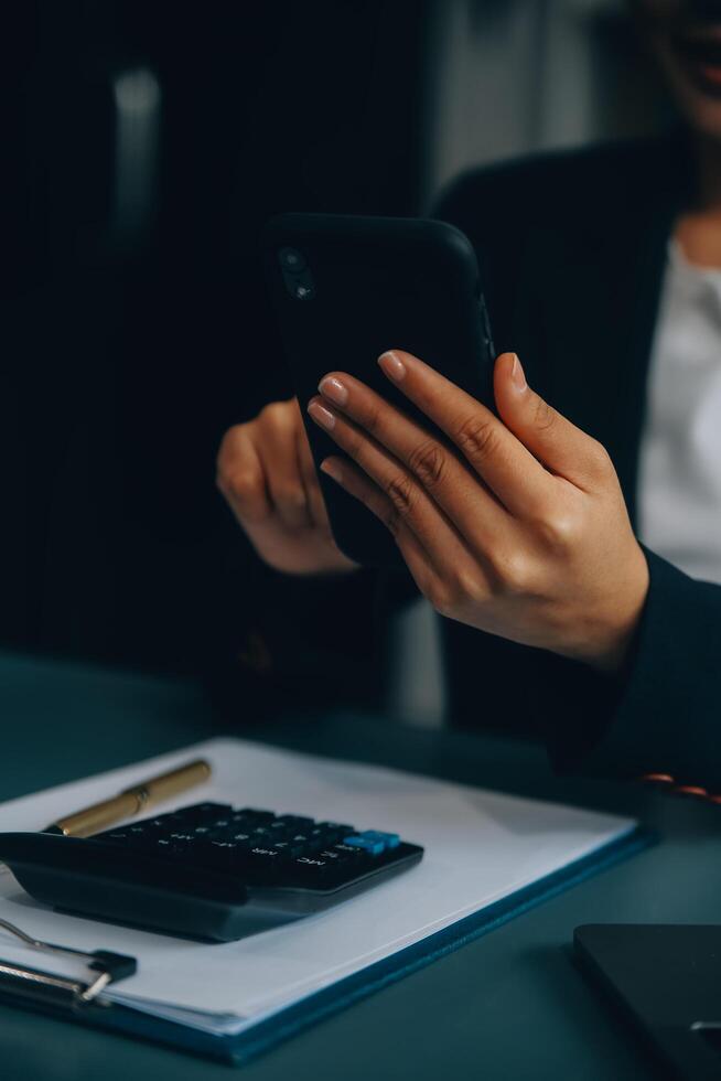 hispanique femme d'affaires dans formel tenue dans sa Bureau content et de bonne humeur tandis que en utilisant les smartphones et fonctionnement. Jeune femme d'affaires en utilisant applications sur cellule Téléphone (s, en train de lire nouvelles, vite lien photo