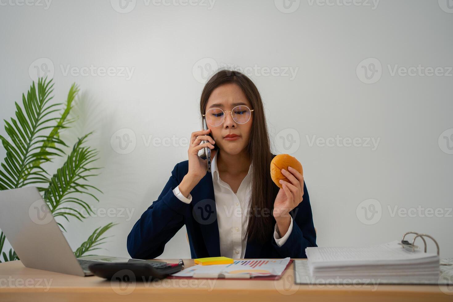 occupé et fatigué femme d'affaires en mangeant pain et Lait pour le déjeuner à le bureau Bureau et travail à livrer financier déclarations à une chef. surmené et mauvais pour la santé pour prêt repas, Burnout concept. photo
