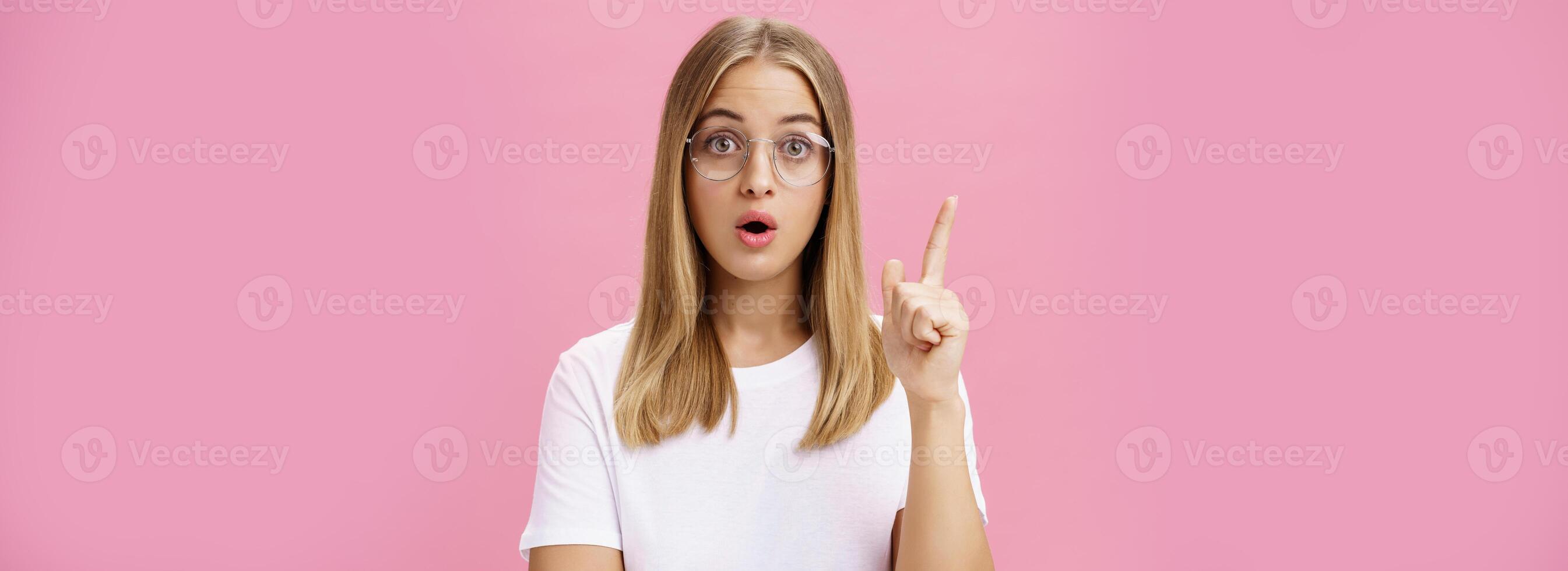 un plus chose avoir besoin a dit. intelligent et intelligent femelle une étudiant dans des lunettes et blanc T-shirt ouvert bouche et pliant lèvres élevage indice doigt dans eureka geste ajouter suggestion, ayant idée photo