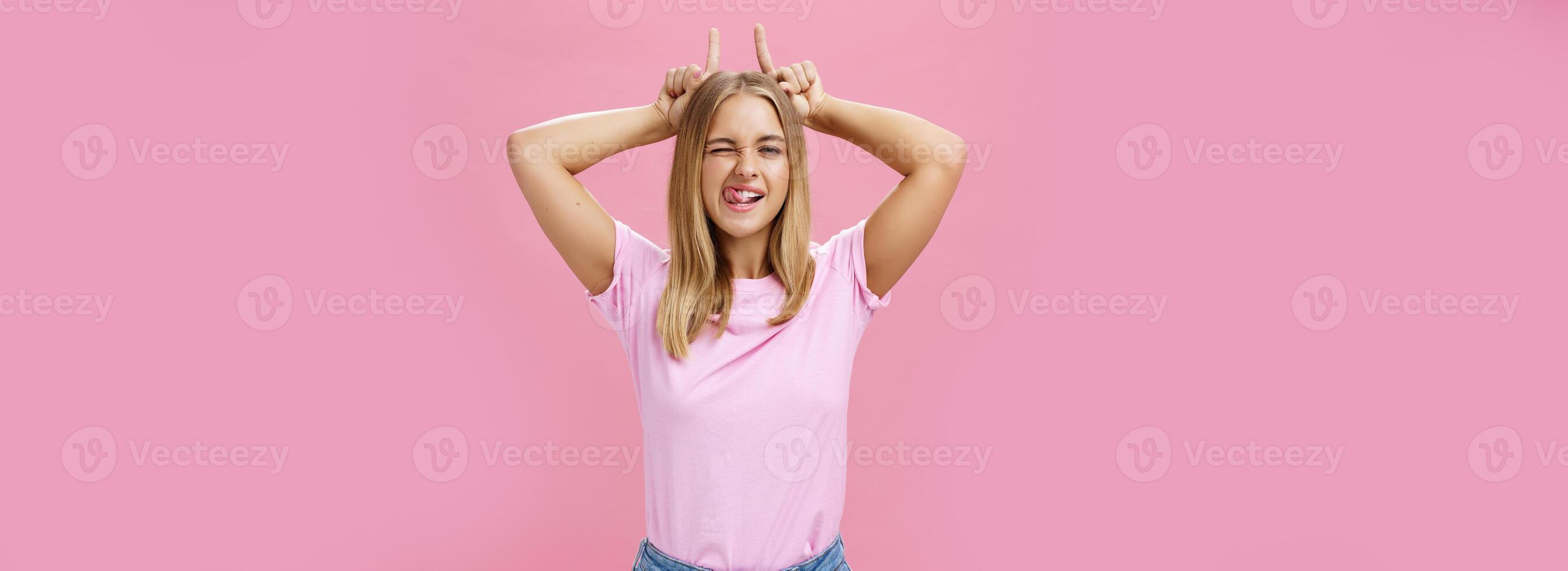 têtu fille jamais laisser vers le bas sur rêves. charmant excité et insouciant optimiste Jeune femme avec bronzer et juste cheveux un clin d'oeil montrant langue ludique en portant indice les doigts sur tête comme cornes photo