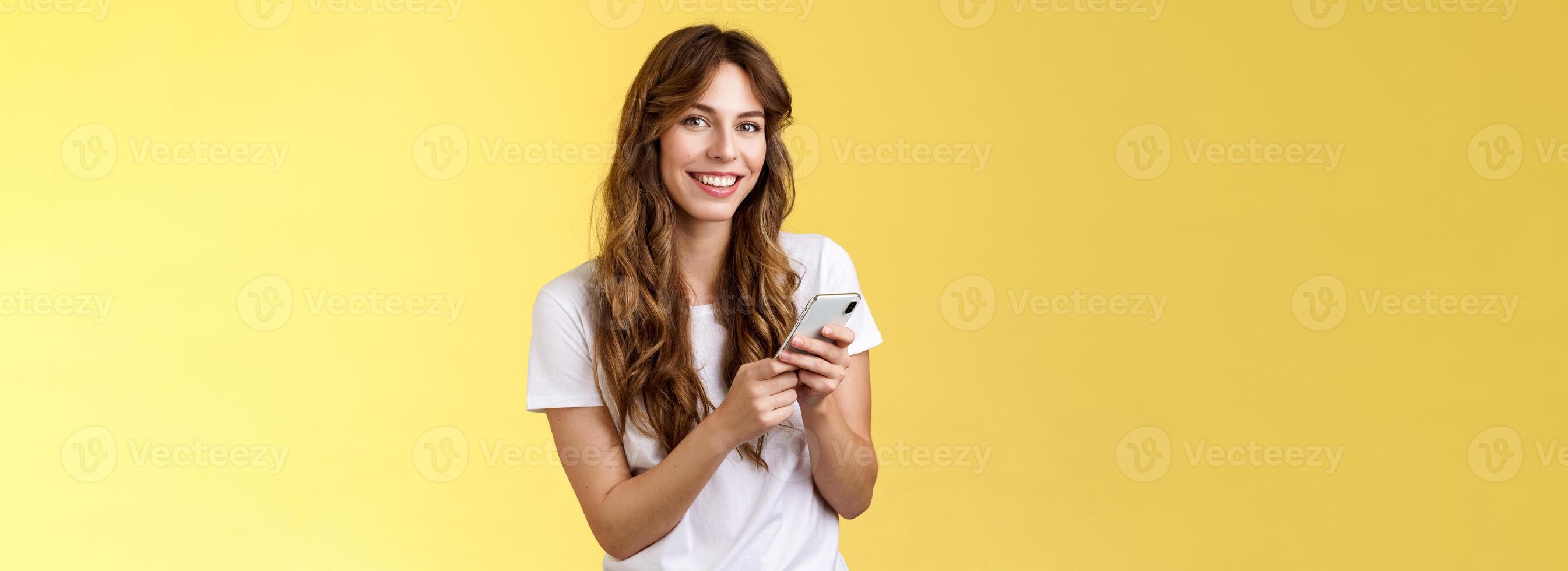 enthousiaste beau Urbain fille porter blanc T-shirt permanent décontractée souriant Enchanté caméra envoyer des SMS tenir téléphone intelligent faire défiler social médias alimentation supporter Jaune Contexte navigation réseau photo