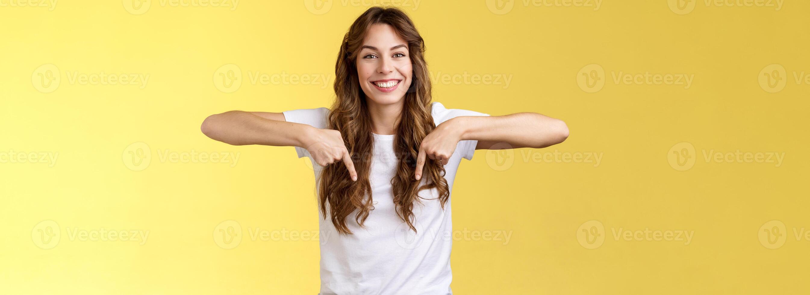 amical de bonne humeur excité content souriant fille longue Naturel brunette la Coupe de cheveux sourire joyeusement montrer du doigt vers le bas indice les doigts spectacle ami génial choix présenter promo Conseil Cliquez sur lien Jaune Contexte photo