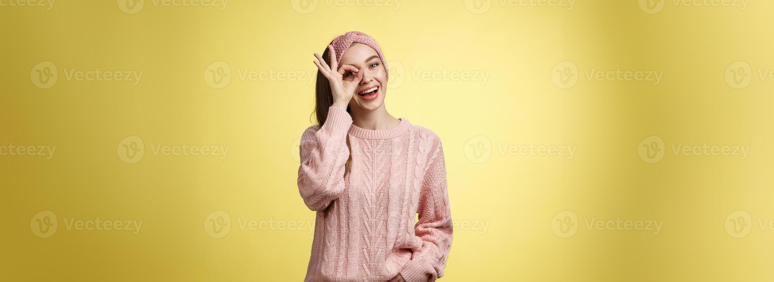 de bonne humeur fille en disant d'accord. attrayant élégant écolière dans tricoté chandail détendu sentiment optimiste, partage bonheur et joie, montrant d'accord signe sur œil souriant optimiste, divertir plus de Jaune mur photo