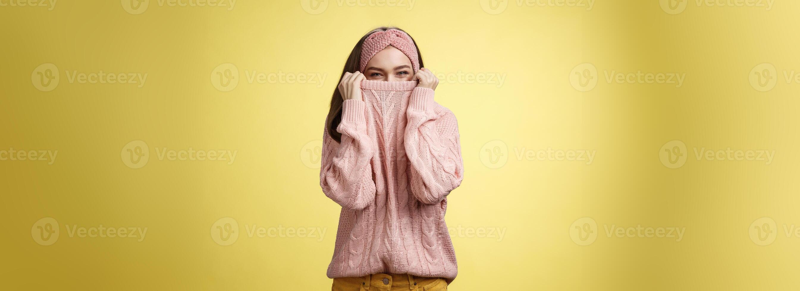 mignonne espiègle Jeune fille cache dans chandail furtivement et plisser les yeux affectueux plus de Haut de tissu tirant collier sur nez, tromper autour ayant amusement Heureusement, étant dans positif bien humeur, échauffement sur du froid journée photo