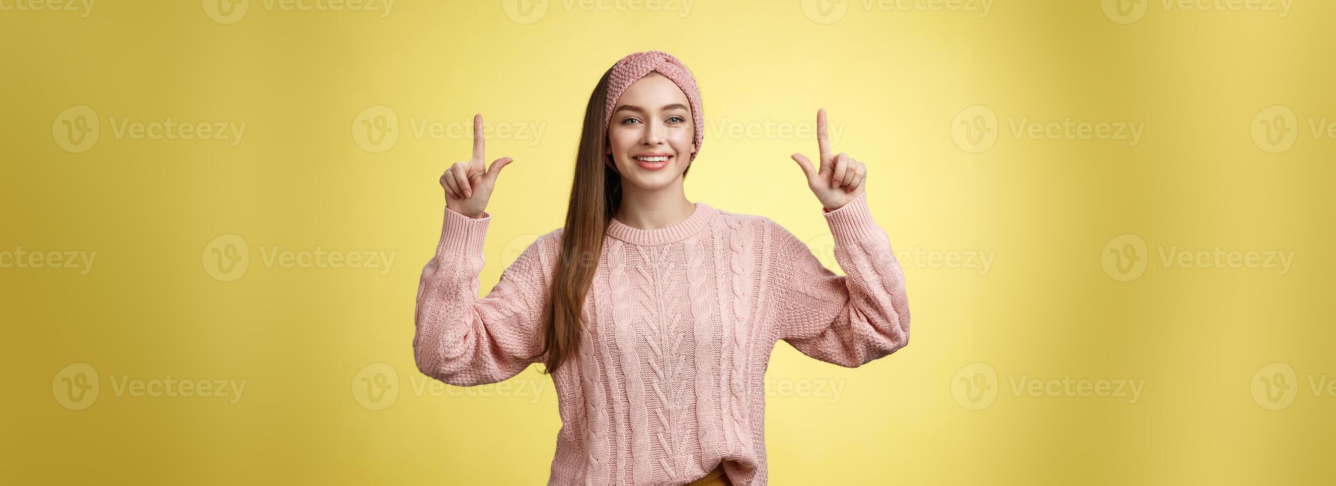 facile à vivre magnifique Jeune femelle étudiant dans tricoté chandail, Bandeau montrer du doigt en haut, promouvoir publicité, souriant Heureusement, sentiment positif posant dans bien humeur, sourire à caméra plus de Jaune mur photo