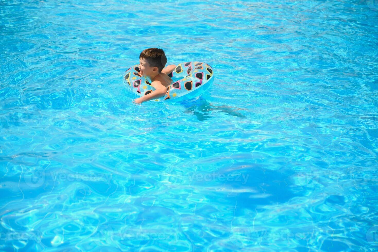 des gamins été vacances. enfant nager dans bassin. des gamins ayant amusement à parc aquatique. marrant garçon sur gonflable caoutchouc cercle. heure d'été. attractions concept photo