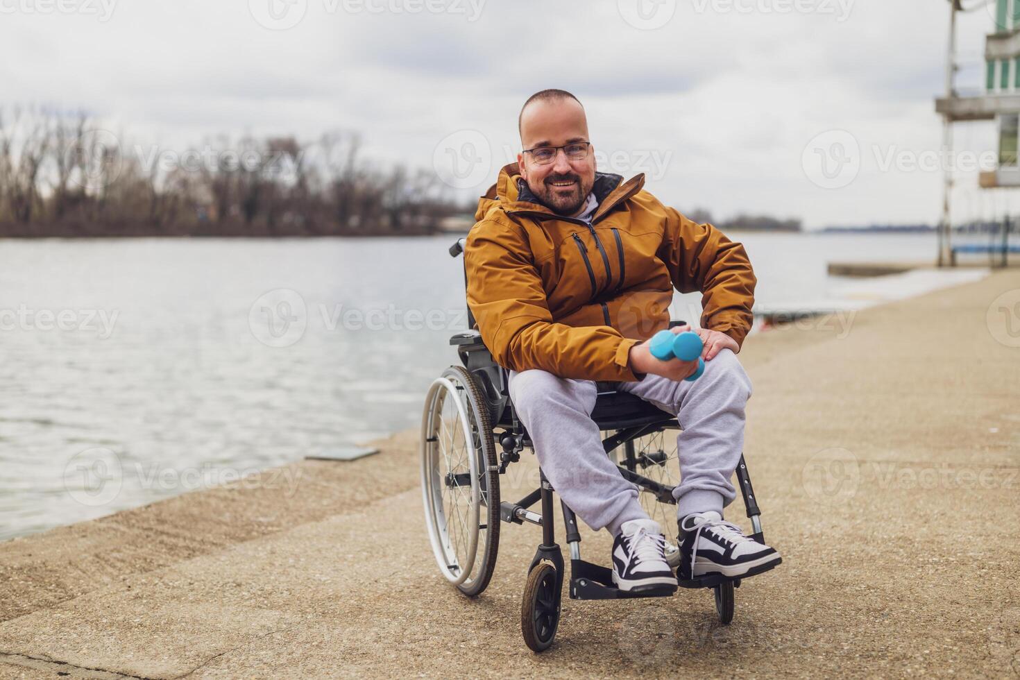 content paraplégique handicapé homme dans fauteuil roulant par le lac. il est prêt pour exercice avec poids. photo