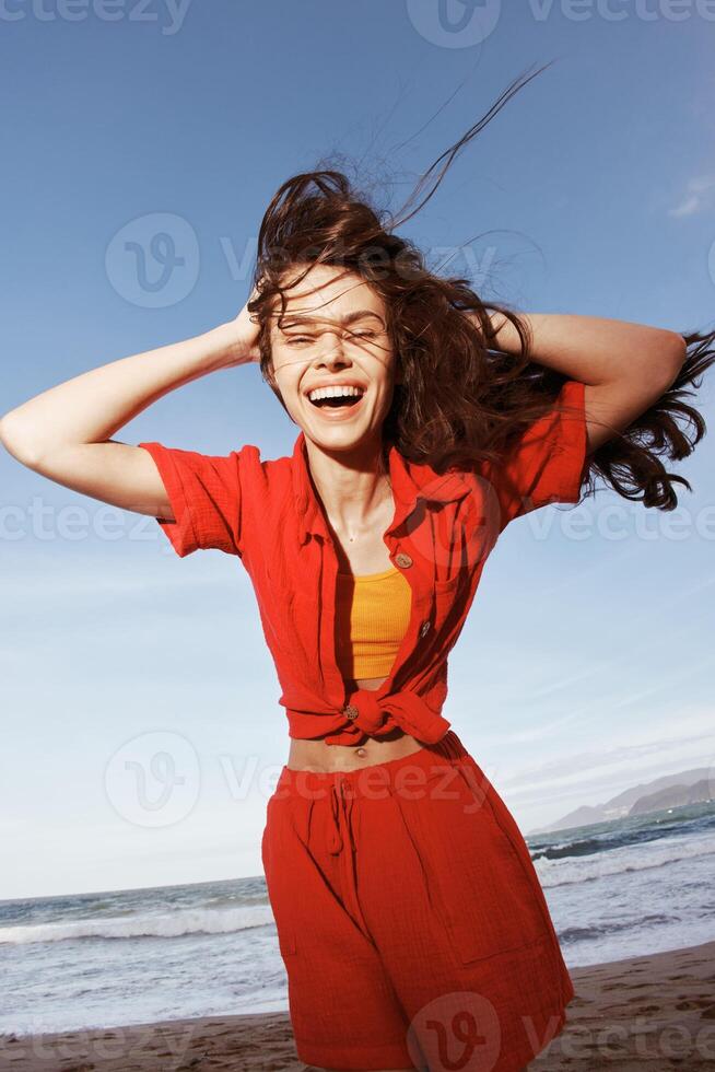 souriant femme dansant avec joie sur une ensoleillé plage, embrassement liberté et profiter été amusement photo