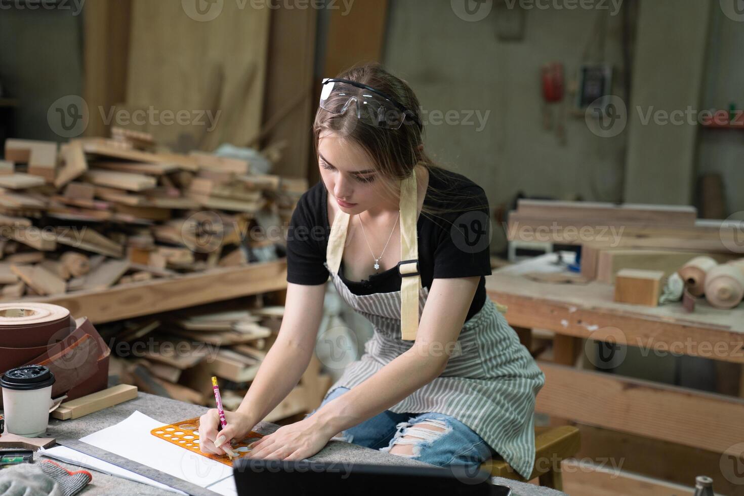 une Jeune femme est formation à être une Charpentier dans le atelier. elle travaux avec une portable ordinateur dans une bois atelier. femelle Charpentier contact les clients par téléphone intelligent. pme photo