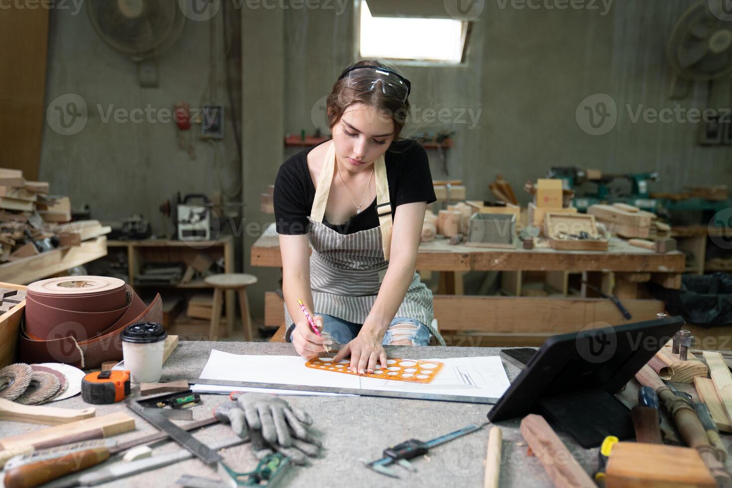 une Jeune femme est formation à être une Charpentier dans le atelier. elle travaux avec une portable ordinateur dans une bois atelier. femelle Charpentier contact les clients par téléphone intelligent. pme ordres, start-up et petit photo