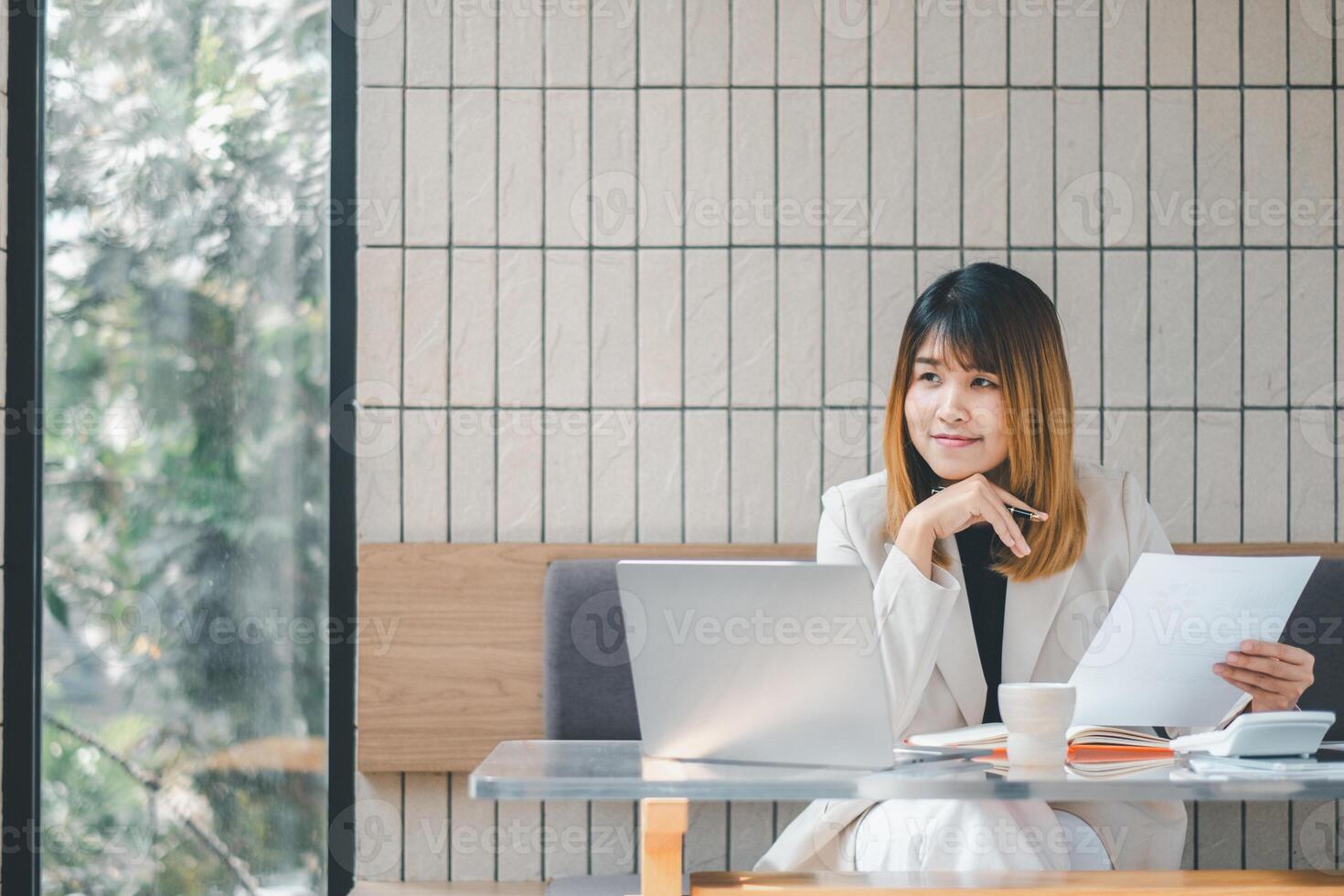 une sur de soi femme d'affaires évalue les documents avec une stylo dans main, portable ouvrir, dans le brillant ambiance de une café paramètre. photo