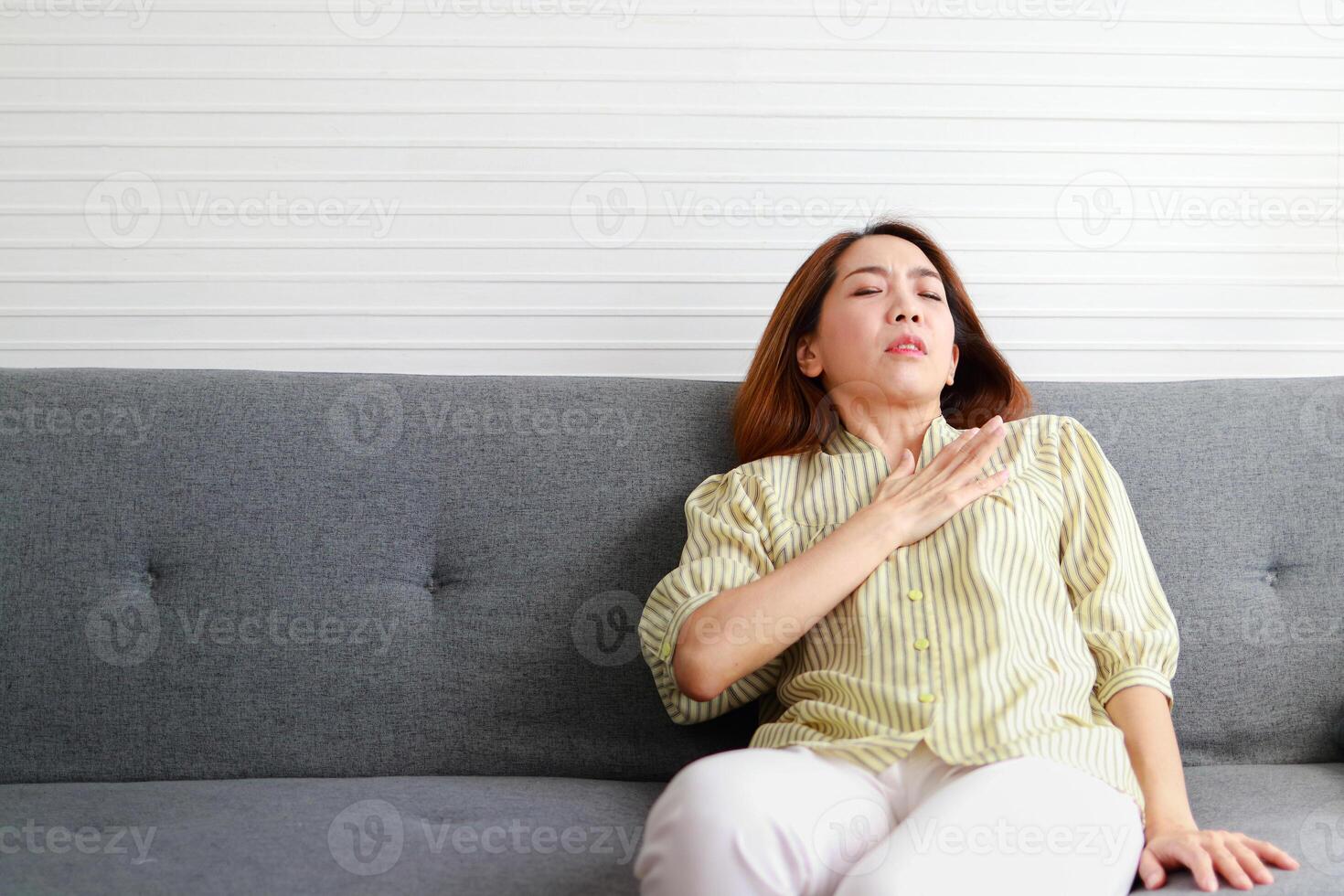 asiatique femme mensonge sur le canapé dans le maison elle avait une tranchant douleur dans sa cœur, comme quelque chose a été pressage sur sa poitrine. elle utilisé sa mains à presse sa poitrine à soulager le douleur. cœur maladie. photo