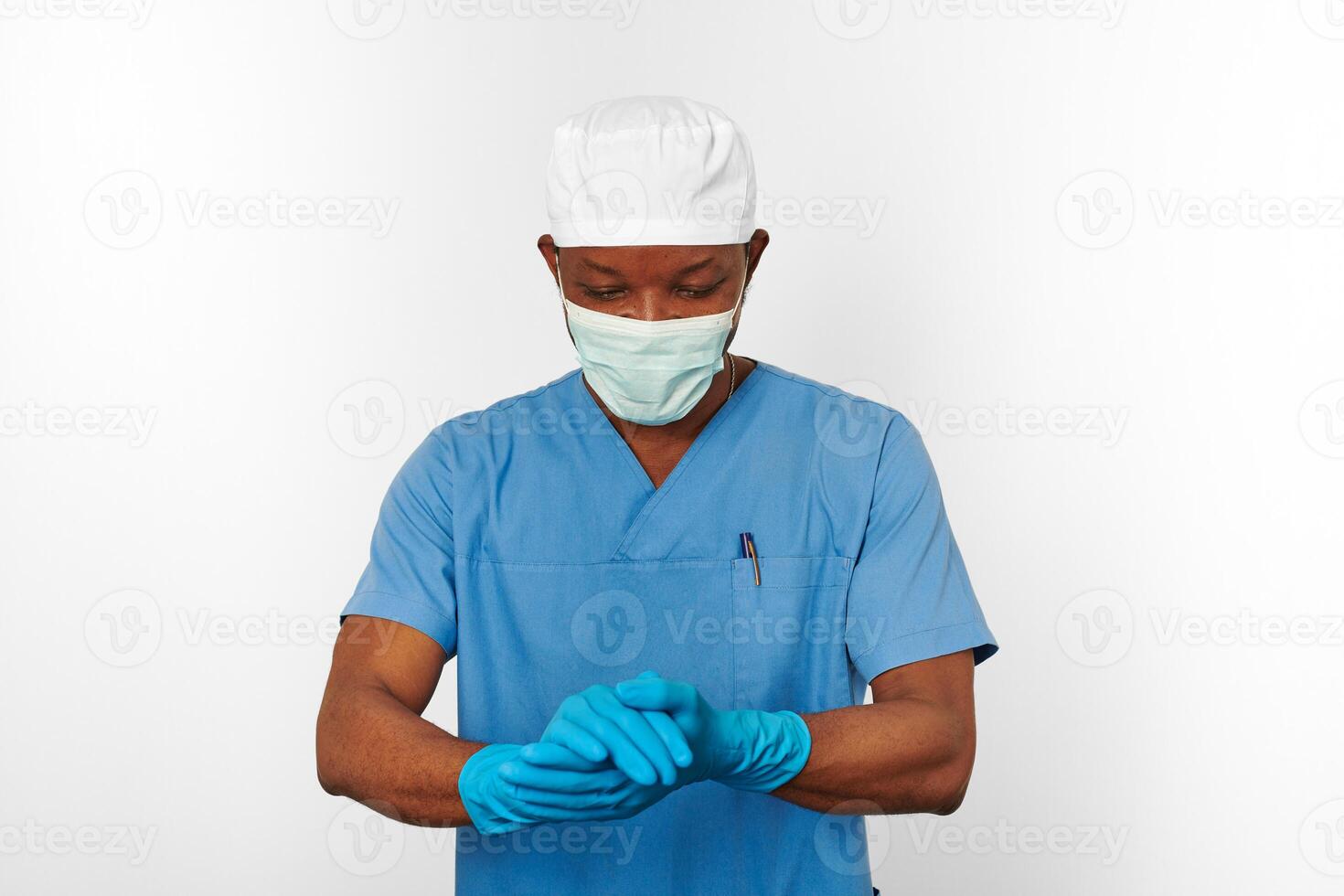 Chirurgien noir médecin homme en manteau bleu casquette blanche masque de chirurgien stérilise des gants bleus fond blanc photo