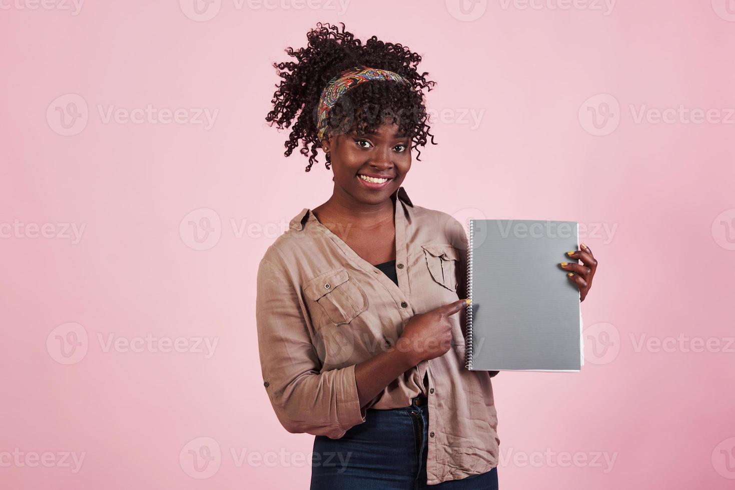 femme tenant un bloc-notes gris dans ses mains sur fond de studio rose photo