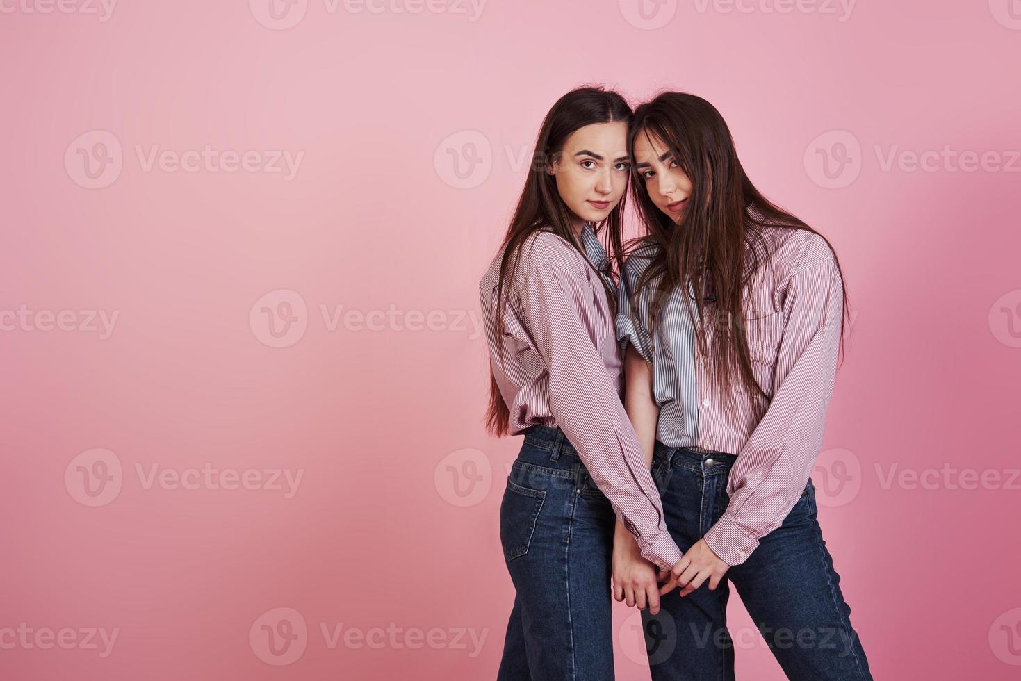 se tenant par les mains. jeunes femmes s'amusant en studio avec fond rose. adorables jumeaux photo