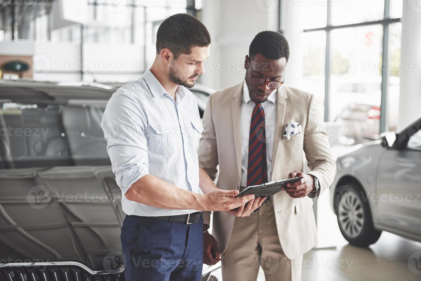 une jeune femme d'affaires noire signe des documents et achète une nouvelle voiture. le concessionnaire automobile se tient à côté de lui photo