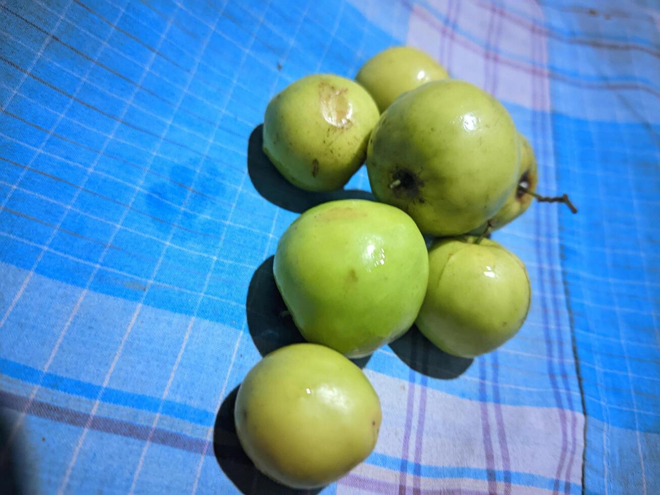 une groupe de vert pommes séance sur une bleu et blanc à carreaux table tissu photo