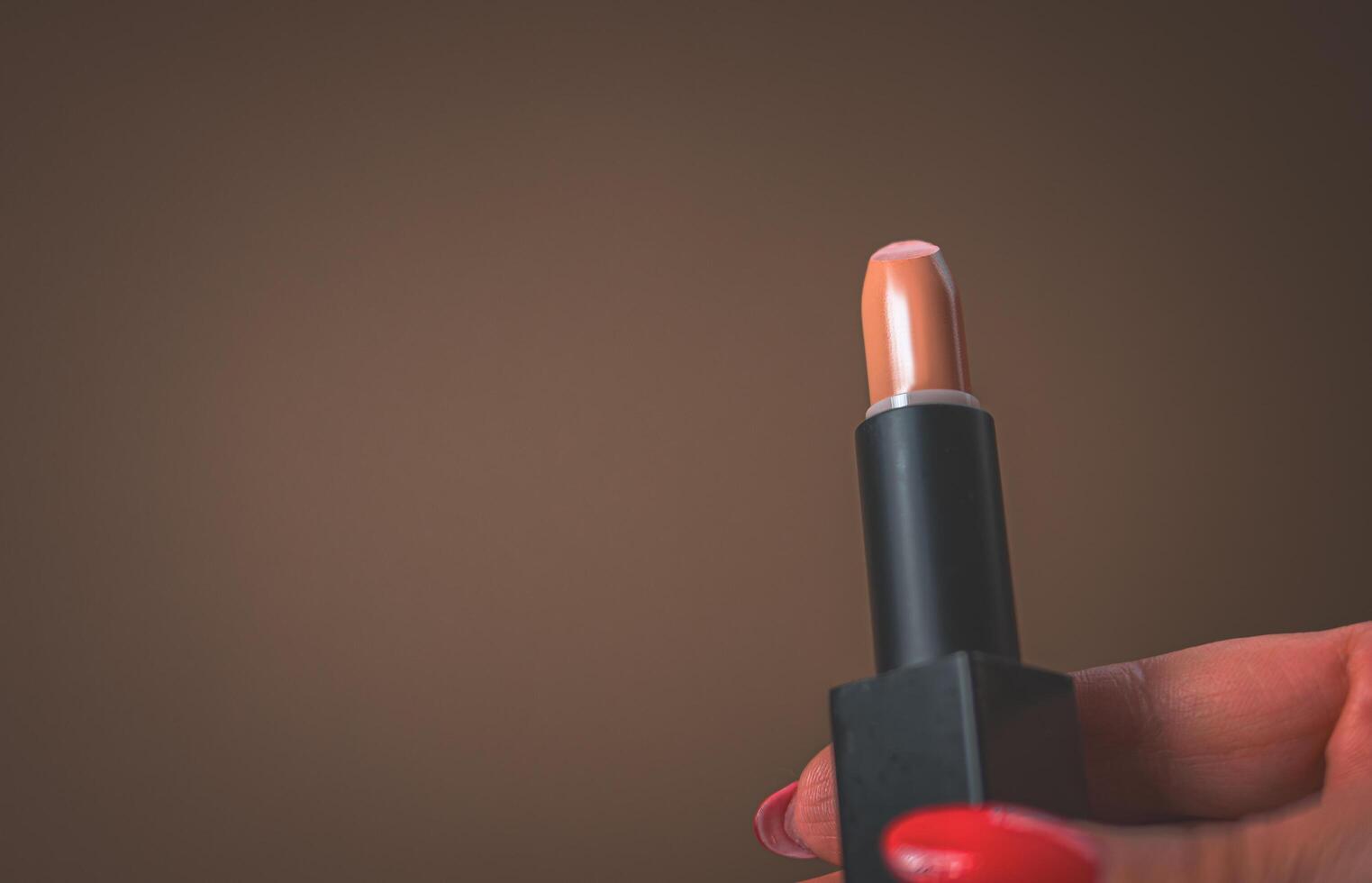 âge se maquiller. rouge rouge à lèvres dans le main de une femme avec une rouge manucure photo