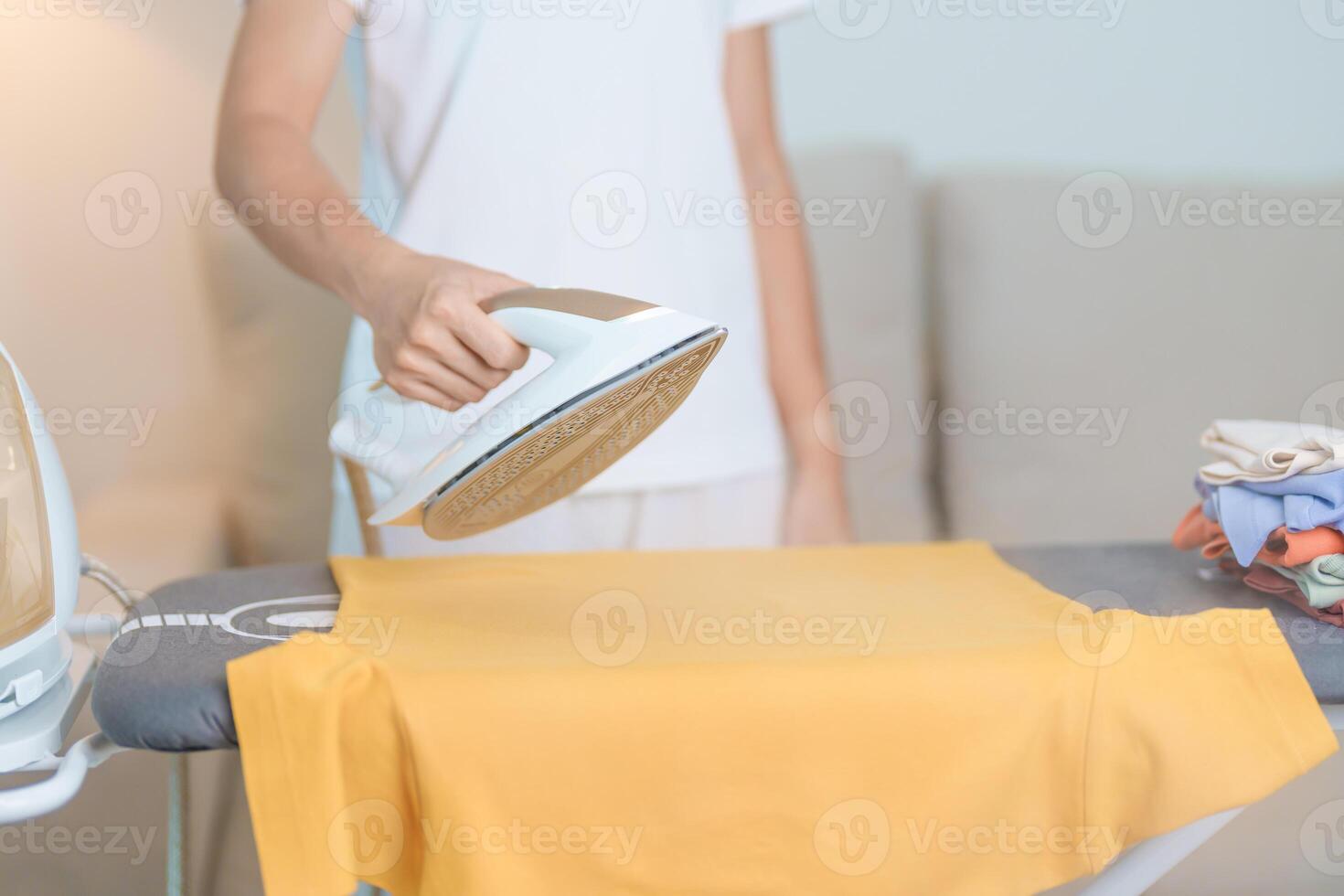 femme tenir électrique chaud le fer presse t chemise vêtements sur repassage conseil, intelligent automatique vapeur fer. blanchisserie, travaux ménagers, Entretien ménager, national hygiène, Ménage de corvées et du quotidien routine concept photo