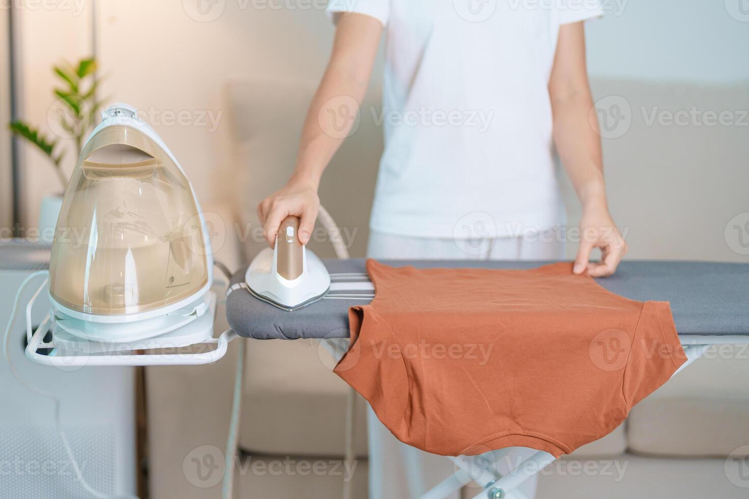 femme tenir électrique chaud le fer presse t chemise vêtements sur repassage conseil, intelligent automatique vapeur fer. blanchisserie, travaux ménagers, Entretien ménager, national hygiène, Ménage de corvées et du quotidien routine concept photo