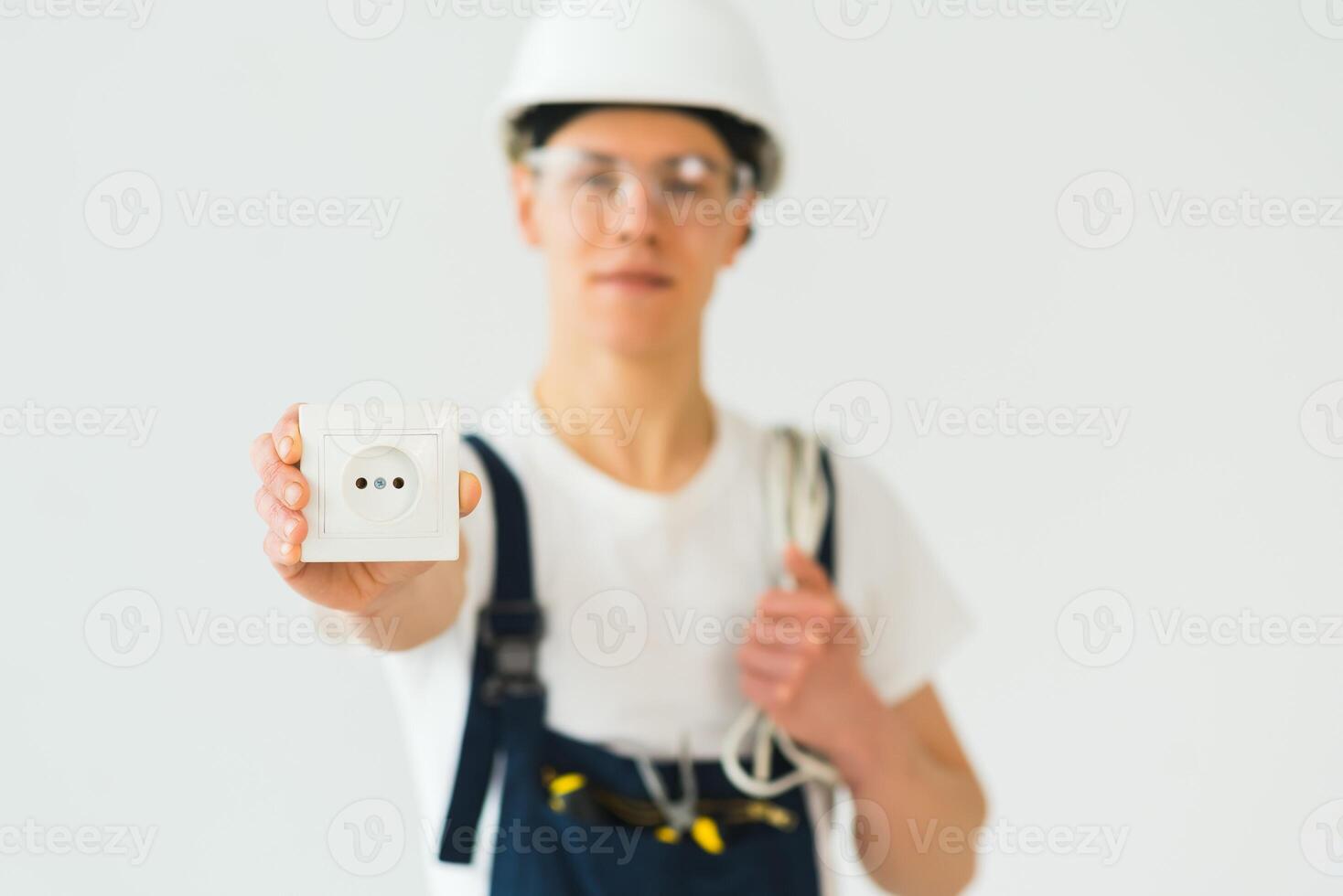 Jeune électricien sur blanc Contexte. détient une câble et prises. photo