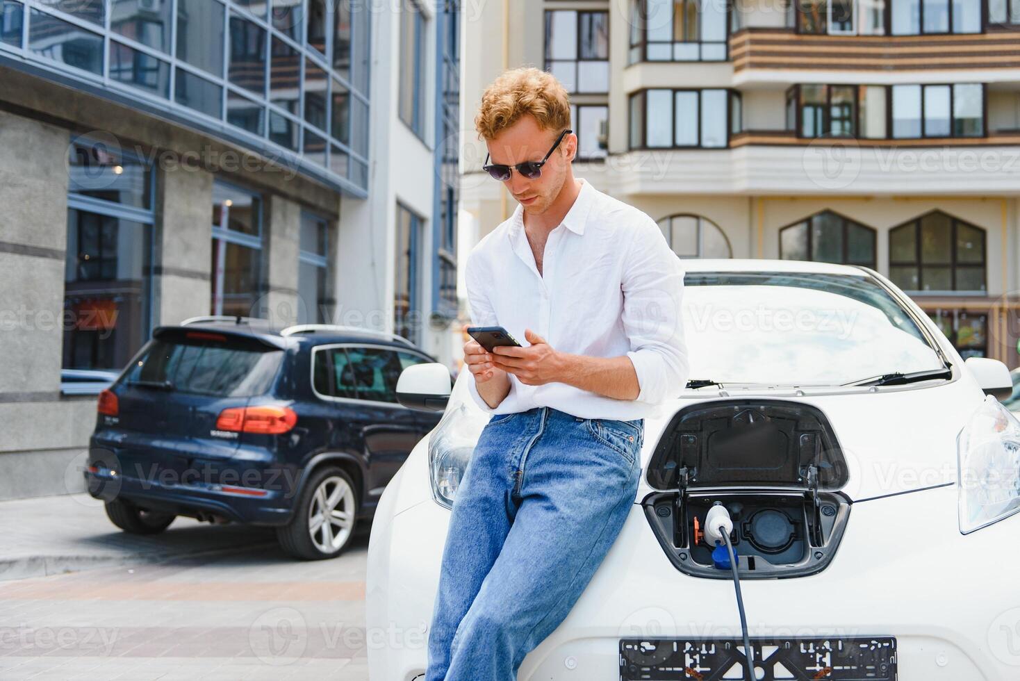 homme avec téléphone intelligent après finition mise en charge de batterie. Masculin près électrique véhicule photo