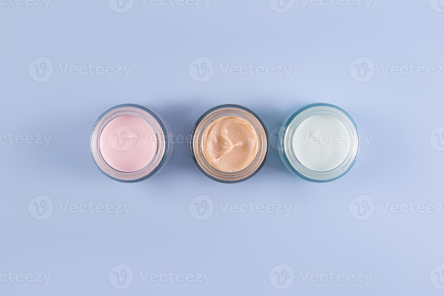 Trois magnifique verre cosmétique pots avec délicat texture de visage et corps se soucier crème sur une bleu Contexte. Haut voir. une copie espace. présentation. photo