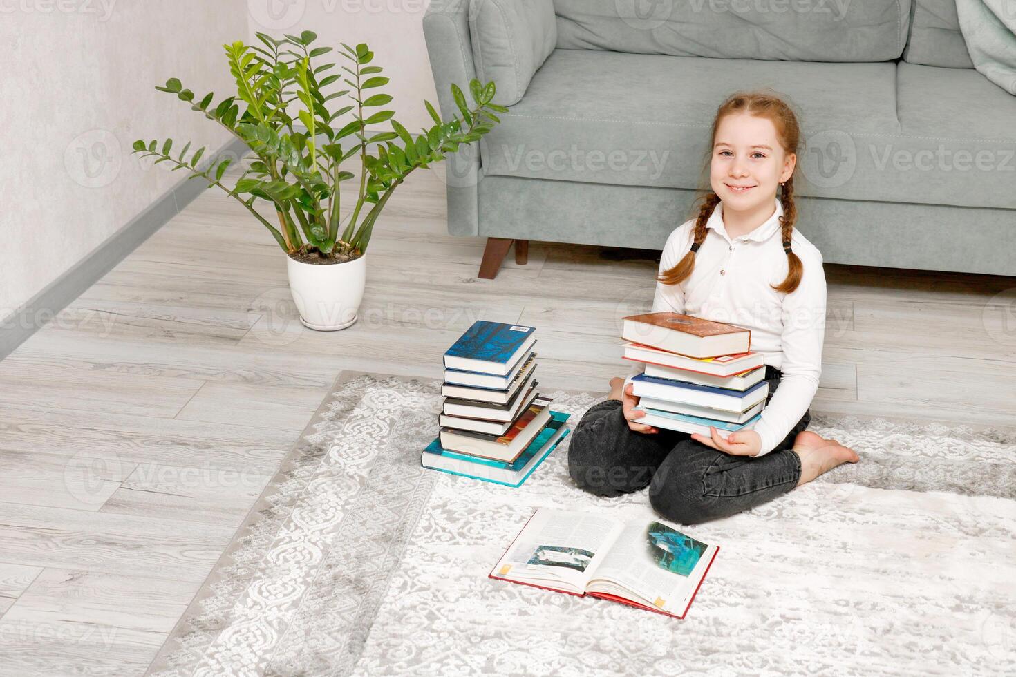mignonne peu fille séance sur le sol à Accueil avec une empiler de livres dans sa mains photo