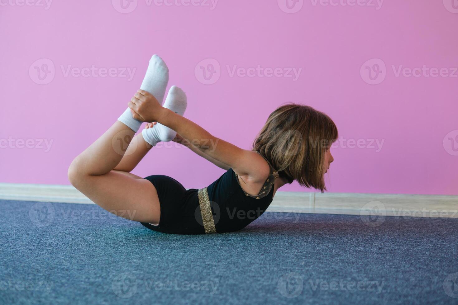 peu fille dans noir spectacles des exercices pour corps souplesse sur une Contexte de une rose mur. le enfant est une gymnaste photo