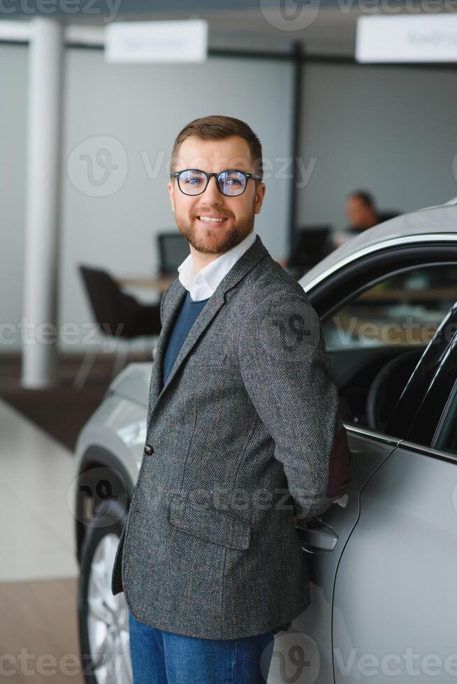 bien en regardant, de bonne humeur et amical vendeur pose dans une voiture salon ou salle d'exposition. photo