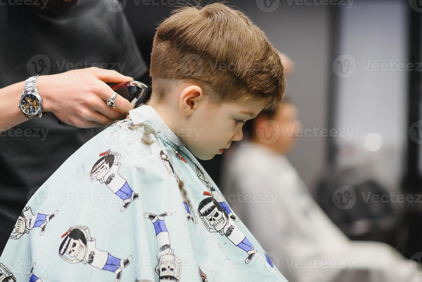 une peu mignonne garçon est assis dans une salon de coiffure à le styliste, une écolier est avoir cheveux Couper dans une beauté salon, une enfant à une chez le coiffeur, une court Pour des hommes la Coupe de cheveux photo