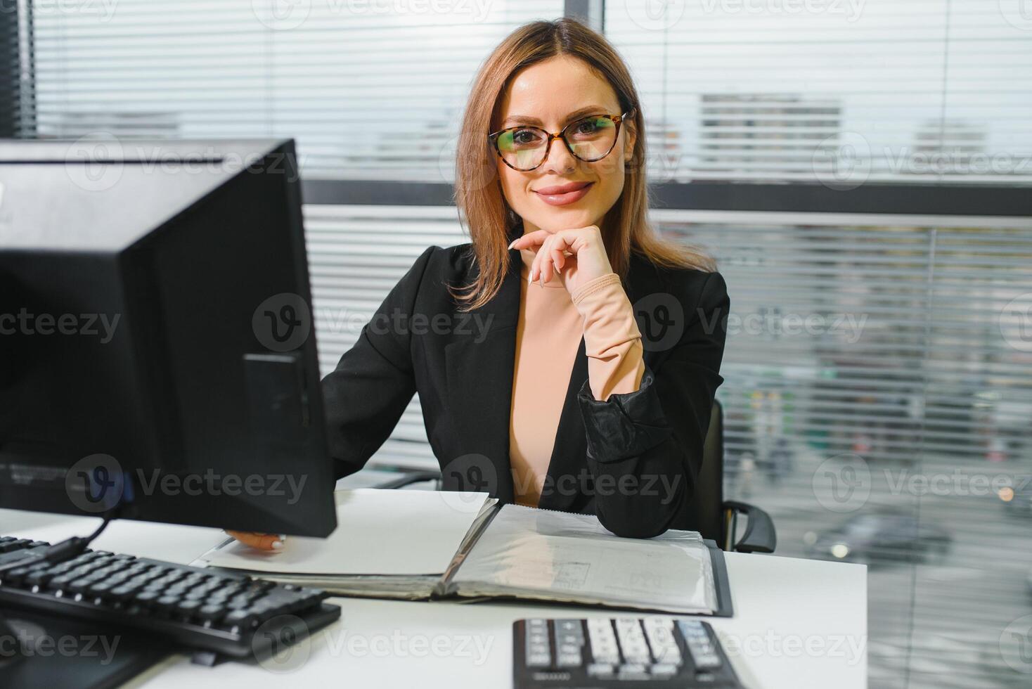 joli, bon, mignon, parfait femme séance à sa bureau sur cuir chaise dans travail gare, portant lunettes, vêtements de cérémonie, ayant portable et carnet sur le table photo