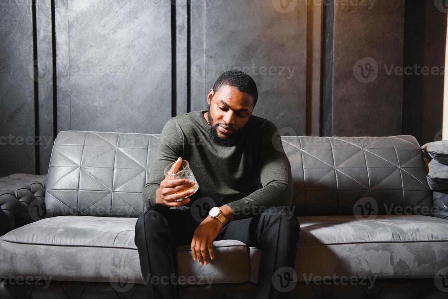 Beau Jeune africain américain homme dans élégant costume avec verre de whisky relaxant sur canapé photo