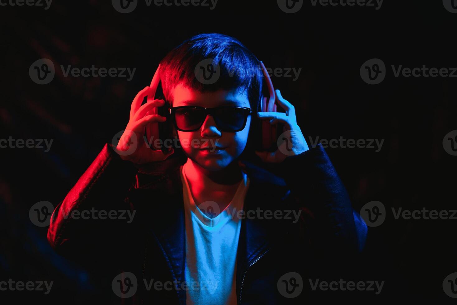 adolescent garçon écoute à la musique avec écouteurs, néon lumière tendance portrait. regards à le caméra photo