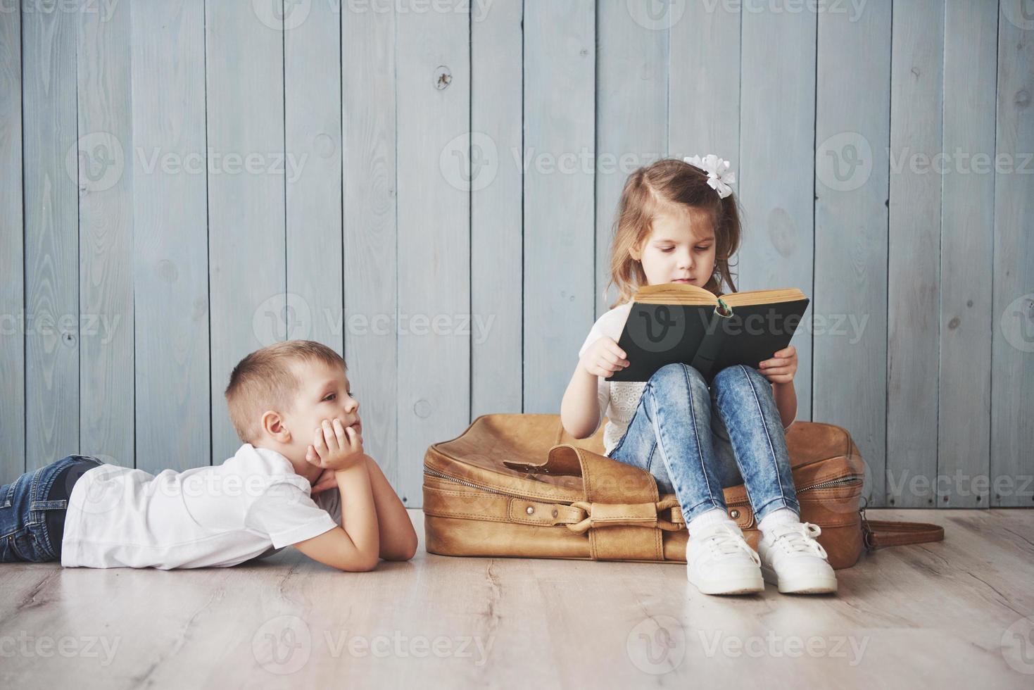 prêt à grand voyage. heureuse petite fille et garçon lisant un livre intéressant portant une grande mallette. concept de liberté et d'imagination photo