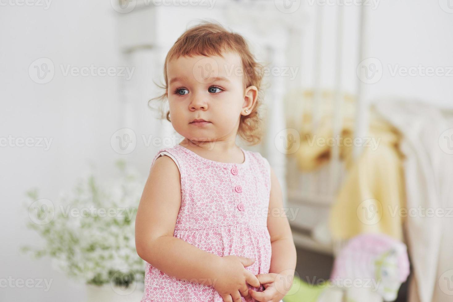 petite fille en robe mignonne implantation au lit jouant avec des jouets à la maison. chambre d'enfant vintage blanche. concept d'enfance photo